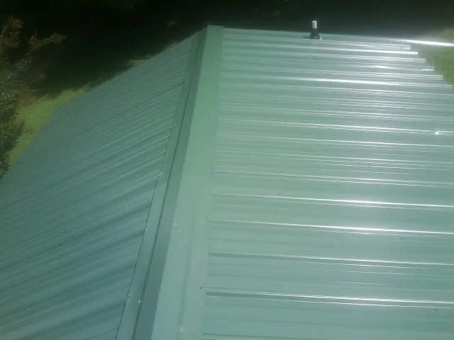 New green metal panels meeting at the ridge of a roof — Flat Roof Repair work by our crew in Liberty